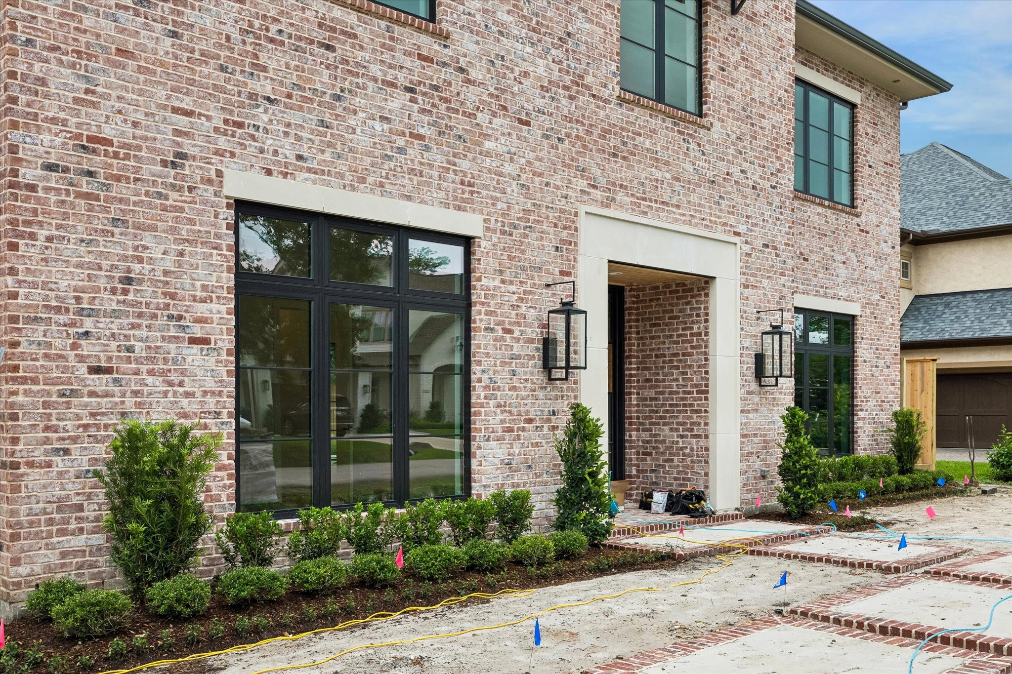 Transitional new construction brick home with clean architectural lines, iron door, gas lanterns and metal awnings. Pictured April 2026.