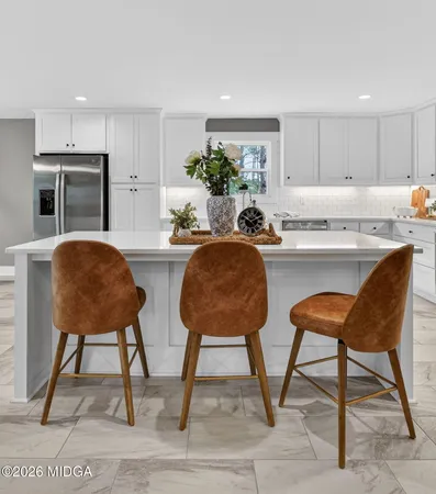 a kitchen with stainless steel appliances kitchen island granite countertop a table chair and a refrigerator