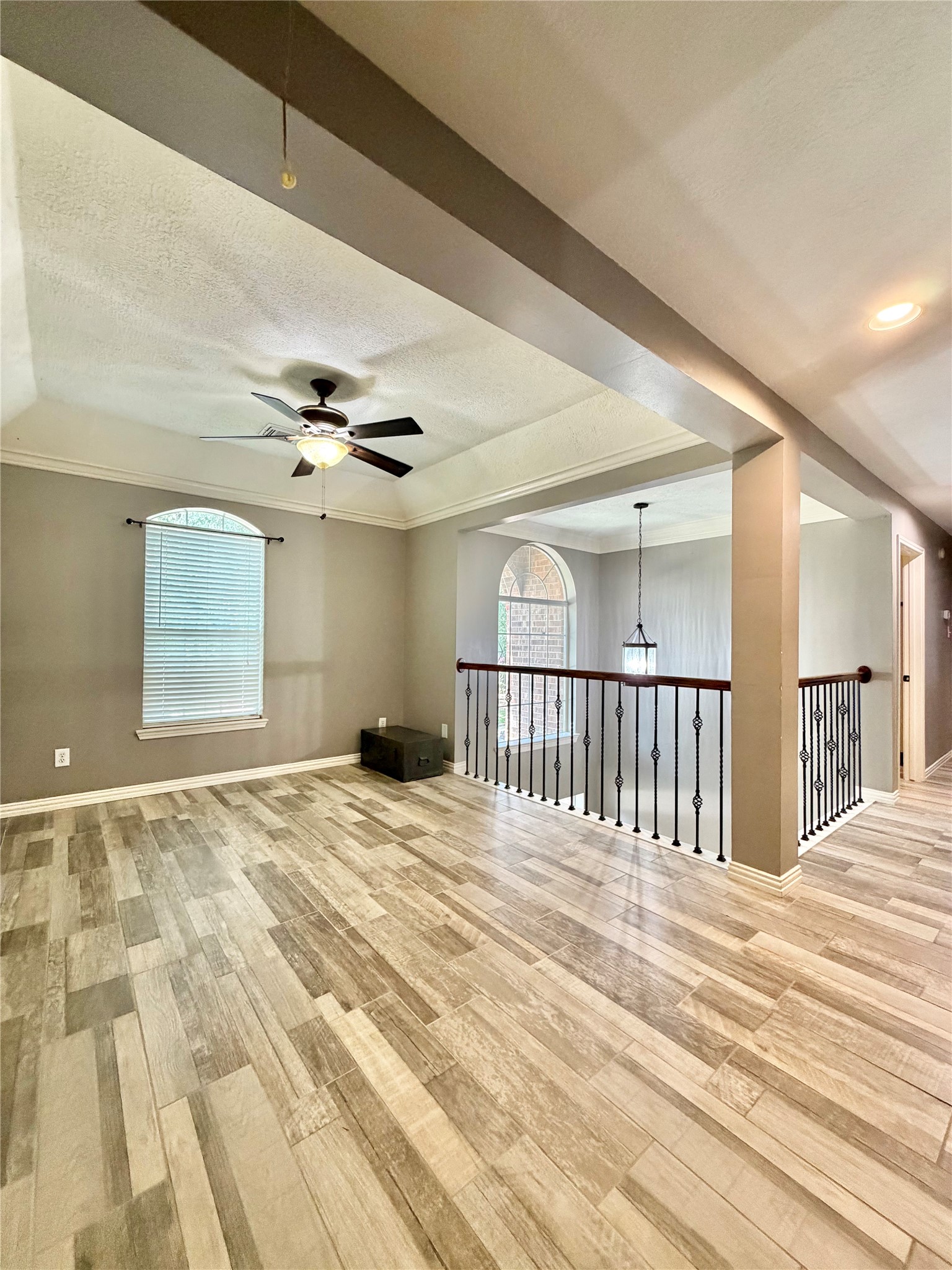 20110 Forest Drive Spring, TX 77388 - Photo 31 of 43 Spacious open area with elegant wood-style flooring, featuring a ceiling fan and large window for natural light. A stylish iron railing overlooks the lower level, adding a touch of sophistication.