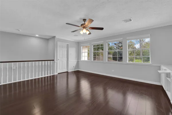 a view of an empty room with wooden floor and a ceiling fan