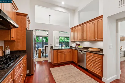 a kitchen with stainless steel appliances granite countertop a refrigerator a sink dishwasher a stove and white cabinets with wooden floor