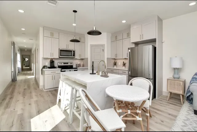 a kitchen with stainless steel appliances kitchen island granite countertop a refrigerator a stove a sink a dining table and chairs with wooden floor