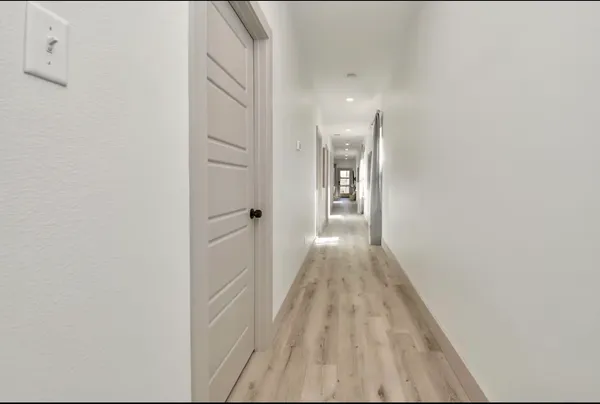 a view of a hallway with wooden floor and a bathroom