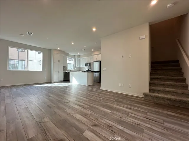 a view of empty room with wooden floor and kitchen