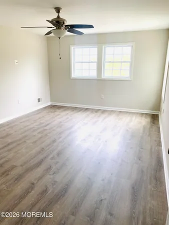 an empty room with wooden floor ceiling fan and windows
