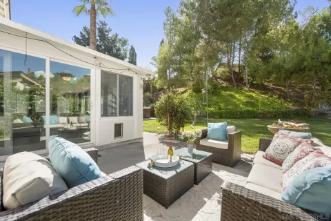 a view of a patio with couches and a table and chairs with floor to ceiling window plants and trees