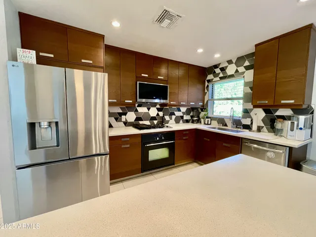 a kitchen with stainless steel appliances granite countertop a refrigerator a sink a stove a microwave a center island and couches