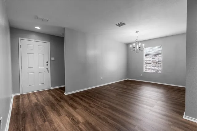 an empty room with wooden floor chandelier and windows