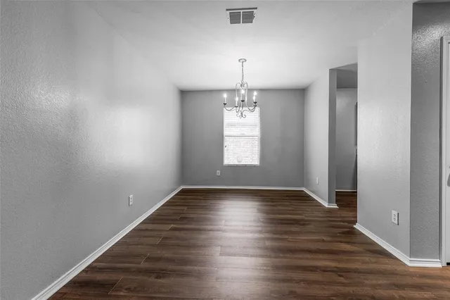 an empty room with wooden floor chandelier and windows