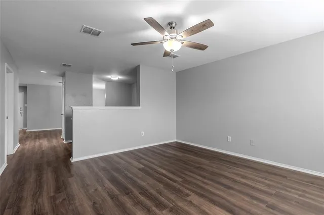 a view of an empty room with wooden floor and a ceiling fan