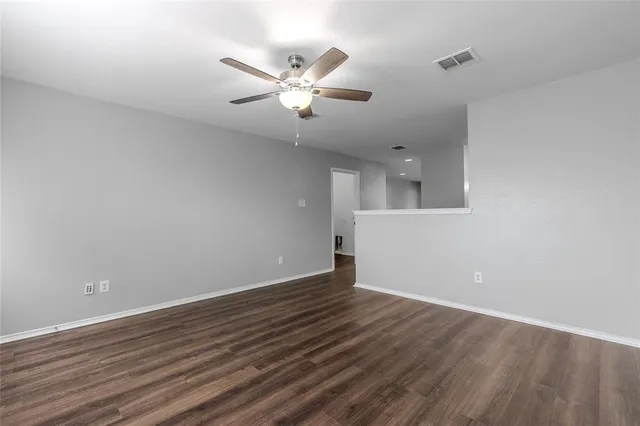 a view of an empty room with wooden floor and a ceiling fan