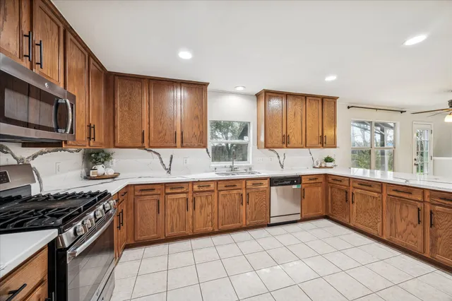 a large kitchen with stainless steel appliances granite countertop a stove top oven a sink dishwasher and white cabinets with wooden floor
