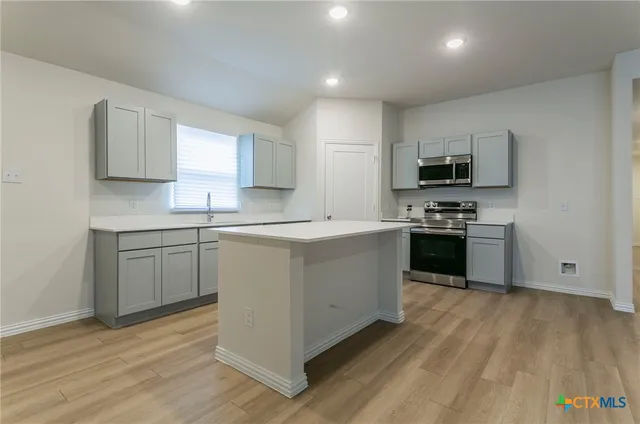 a kitchen with stainless steel appliances a sink dishwasher a stove top oven a refrigerator with grey cabinets and wooden floor