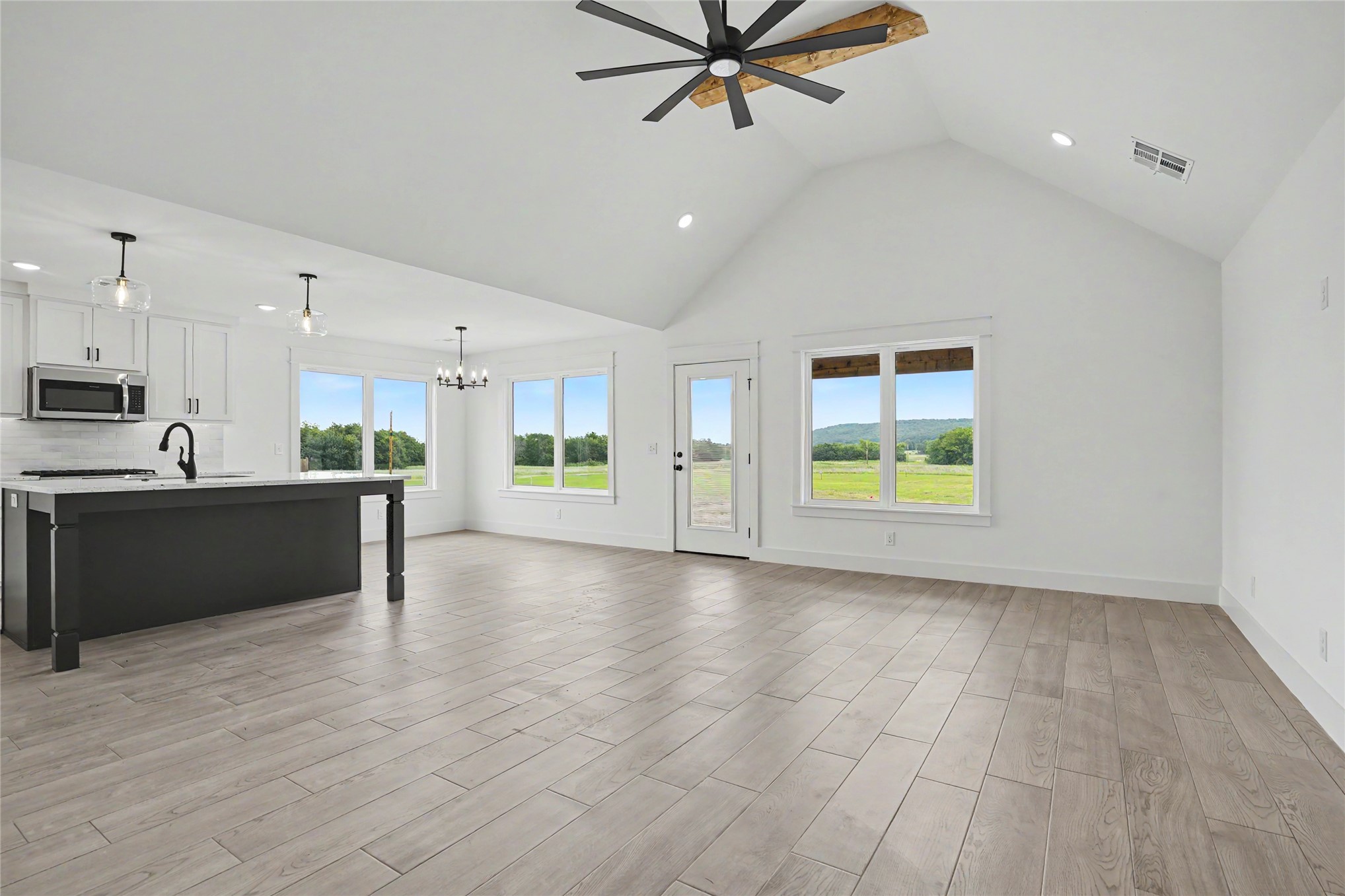 Open-concept living space featuring vaulted ceilings, wood-finish flooring, and a kitchen island with pendant lighting