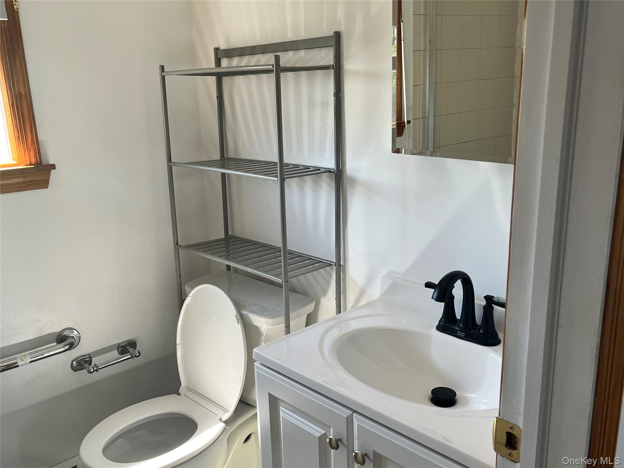 4278 Clarissa Road Bethpage, NY 11714 - Photo 7 of 9 Bathroom featuring a white vanity with a dark faucet, mirror, toilet, and chrome grab bar