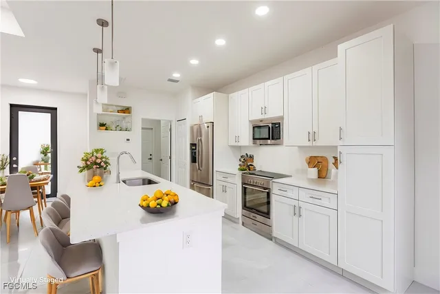 a kitchen with stainless steel appliances kitchen island granite countertop a refrigerator a stove a sink dishwasher and white cabinets with wooden floor