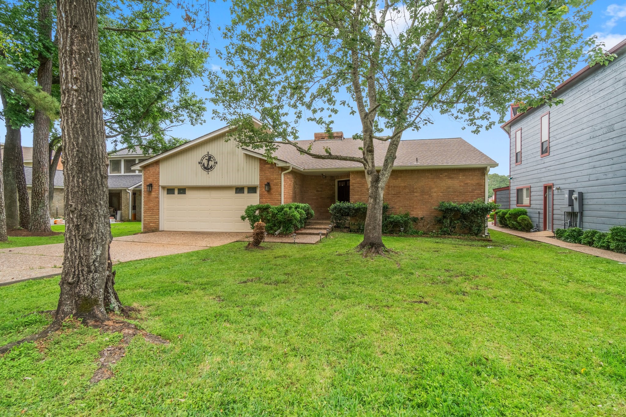 Charming single-story brick home with a two-car garage, set on a lush green lawn with mature trees. The inviting exterior features a well-maintained facade and a spacious driveway.