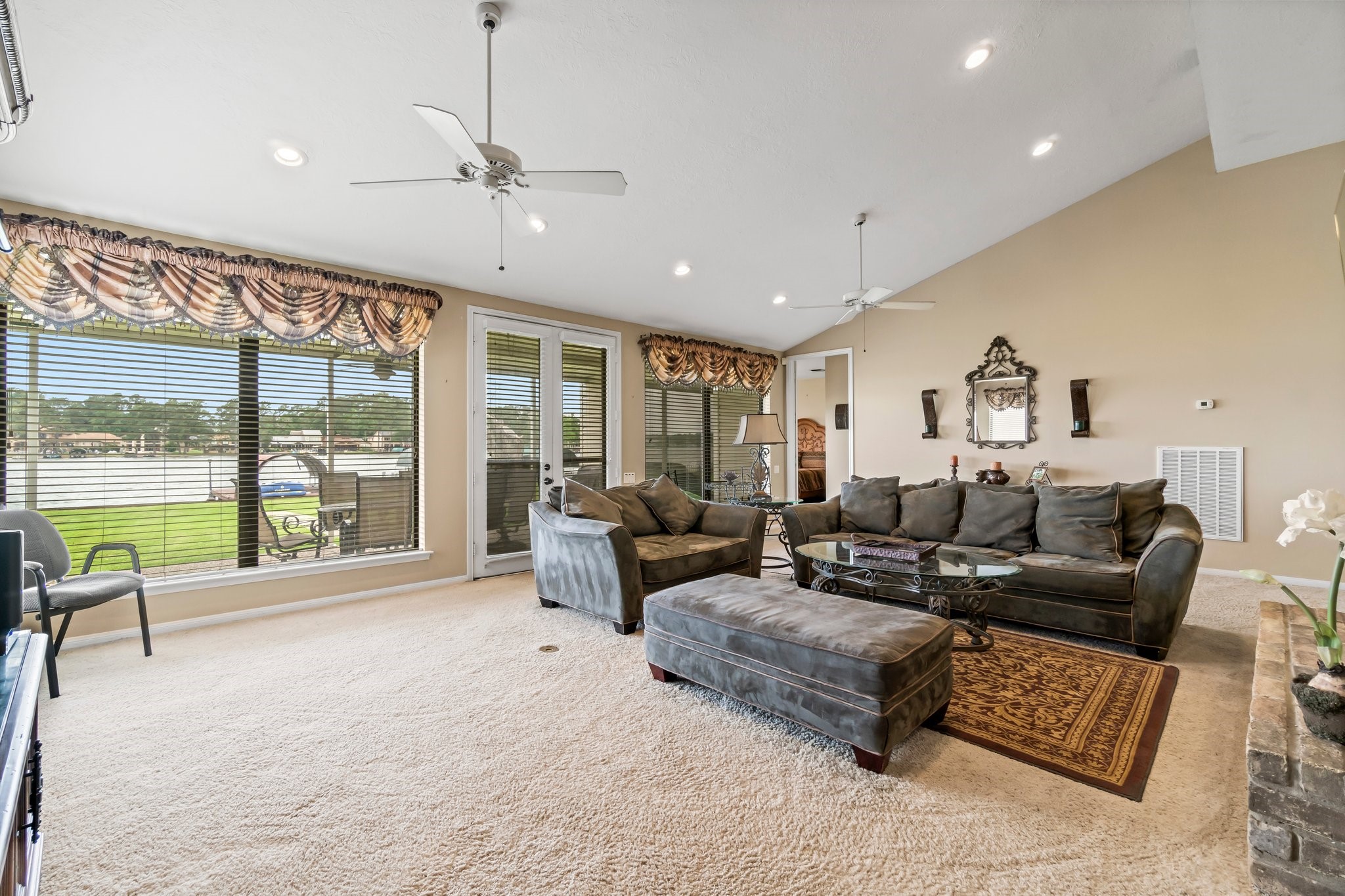 2839 Hemingway Drive Montgomery, TX 77356 - Photo 16 of 49 This spacious living room features vaulted ceilings, plush carpeting, and large windows with elegant drapery, providing ample natural light. It includes cozy seating, a stylish area rug, and a decorative mirror, creating a welcoming and comfortable atmosphere.