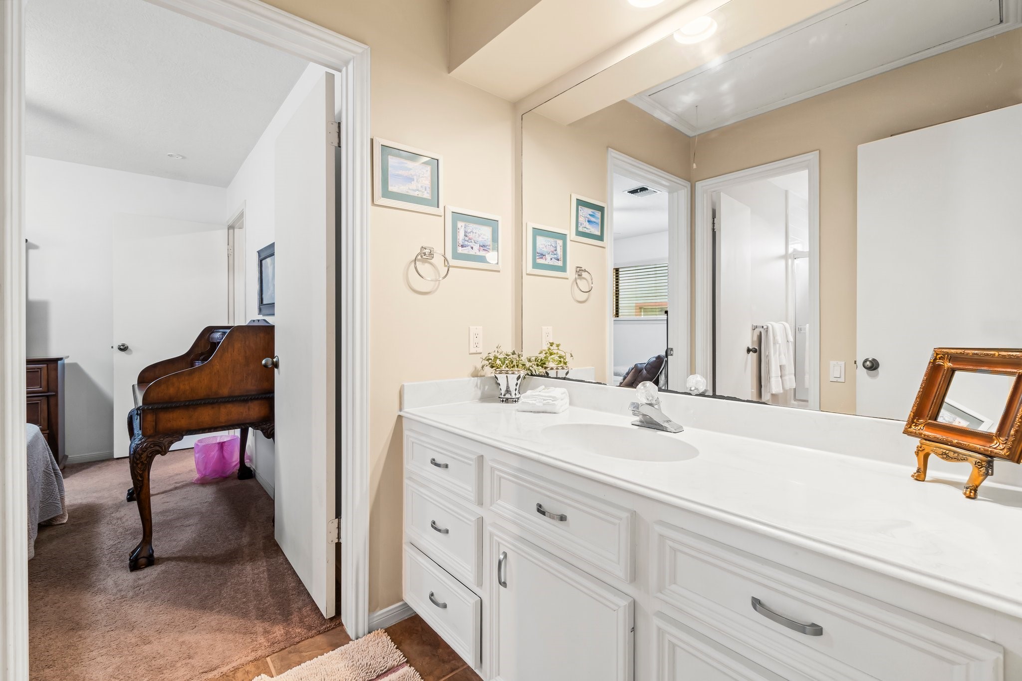 2839 Hemingway Drive Montgomery, TX 77356 - Photo 22 of 49 This photo showcases a bright bathroom with a large vanity, plenty of storage space, and a wide mirror. The room is connected to an adjoining bedroom, featuring a vintage-style desk. Neutral tones and decorative accents add to the room's appeal.