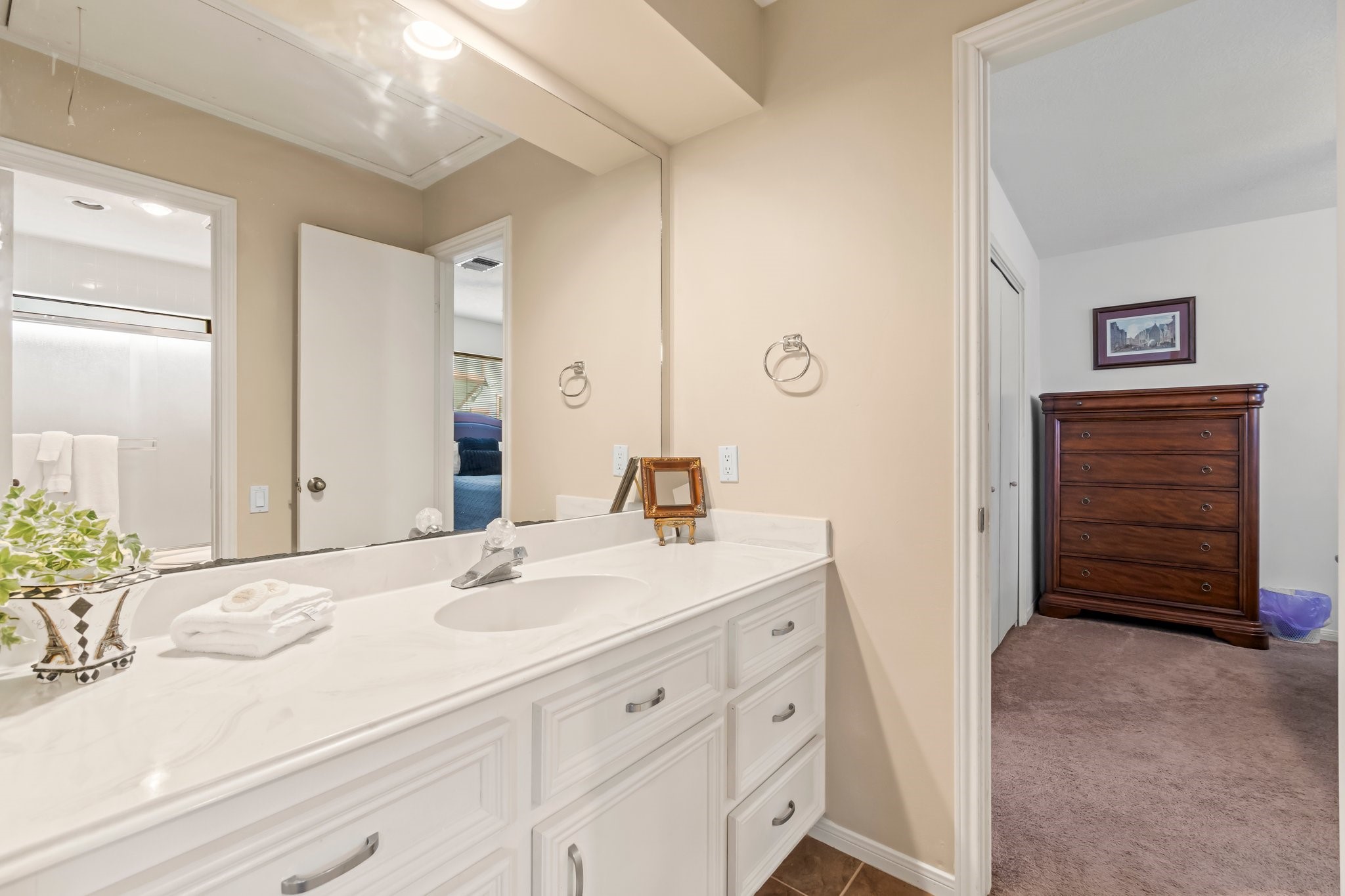 2839 Hemingway Drive Montgomery, TX 77356 - Photo 23 of 49 This photo showcases a bright bathroom with a spacious white vanity and ample storage. It connects to a cozy carpeted bedroom featuring a large wooden dresser.