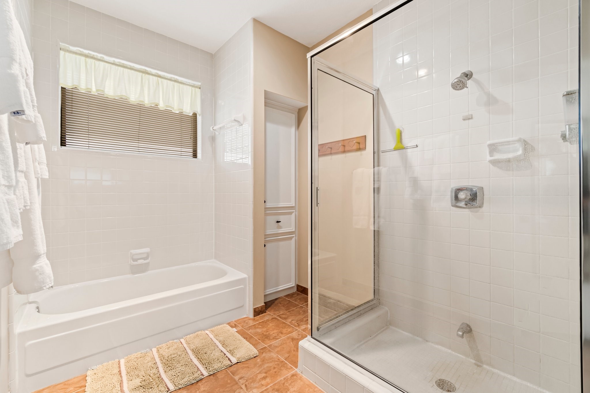 2839 Hemingway Drive Montgomery, TX 77356 - Photo 29 of 49 This bathroom features a bright, clean design with a separate bathtub and glass-enclosed shower. The white tile walls and flooring create a fresh, inviting space, complemented by a window for natural light.