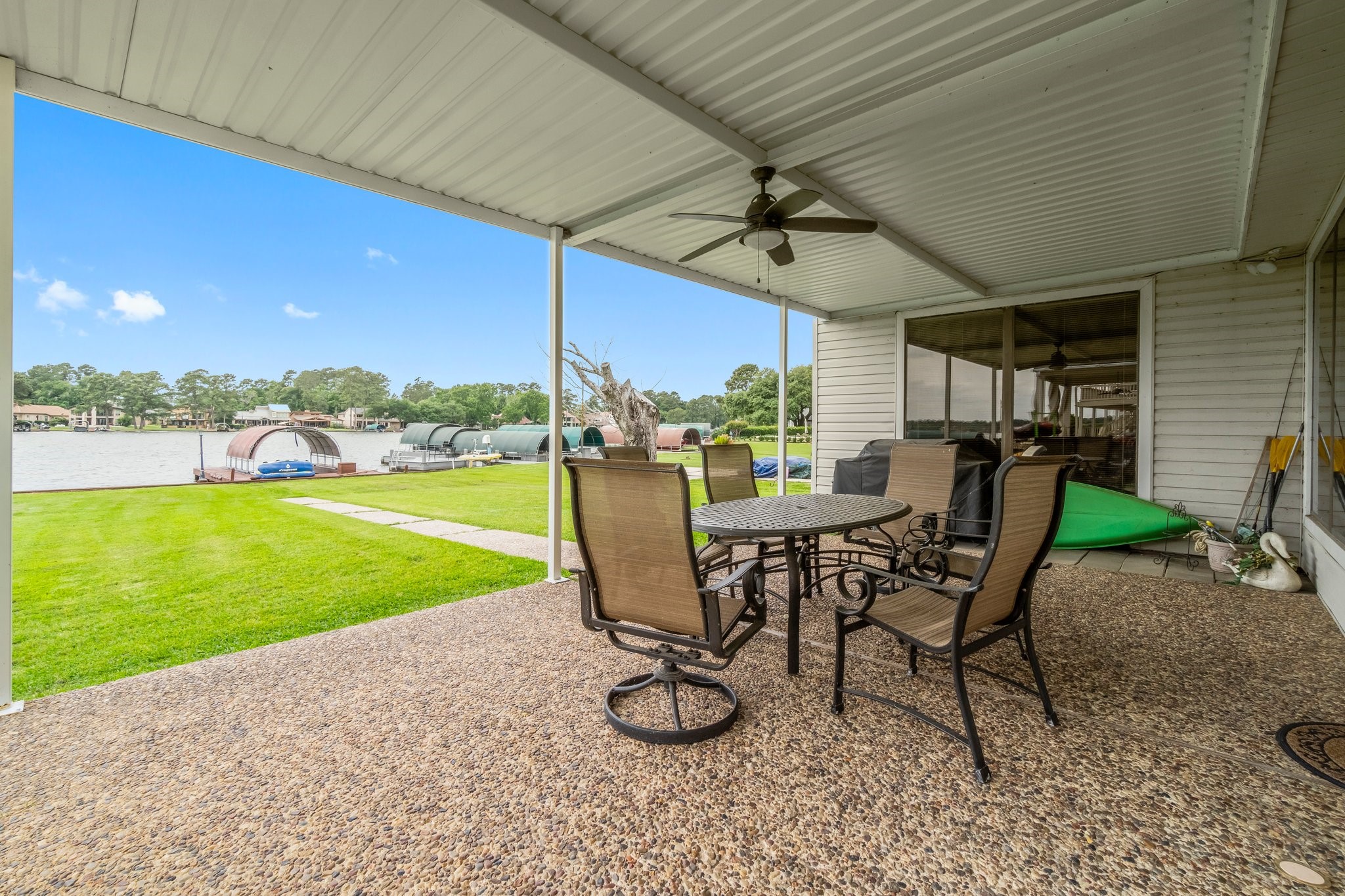 2839 Hemingway Drive Montgomery, TX 77356 - Photo 31 of 49 This photo showcases a covered patio with a fan, featuring a seating area overlooking a lush lawn and a serene lake view. Ideal for outdoor relaxation and entertaining.