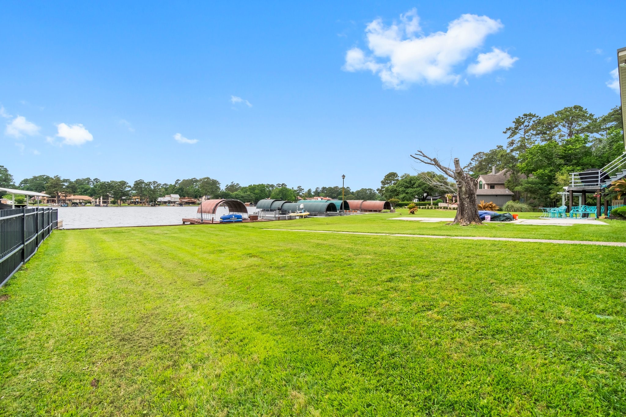 2839 Hemingway Drive Montgomery, TX 77356 - Photo 33 of 49 This photo showcases a spacious, well-maintained lawn with a waterfront view. The property includes a boat dock and is bordered by a fence on one side. It's ideal for outdoor activities and enjoying scenic water views.