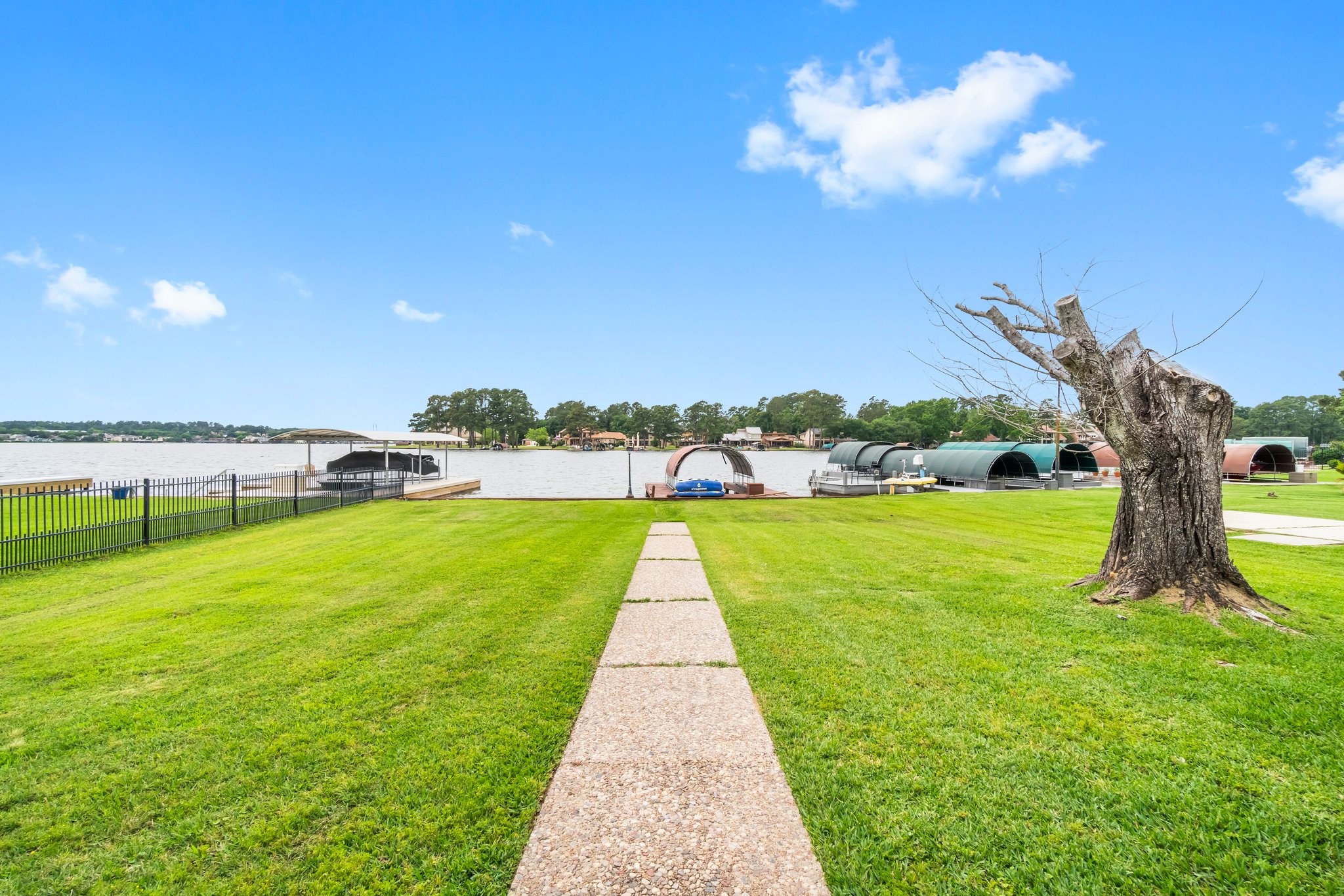 2839 Hemingway Drive Montgomery, TX 77356 - Photo 34 of 49 This photo showcases a spacious, grassy backyard leading to a serene waterfront. A paved walkway guides you towards the water, where boat docks are visible. The area is fenced, offering both security and stunning views of the lake.
