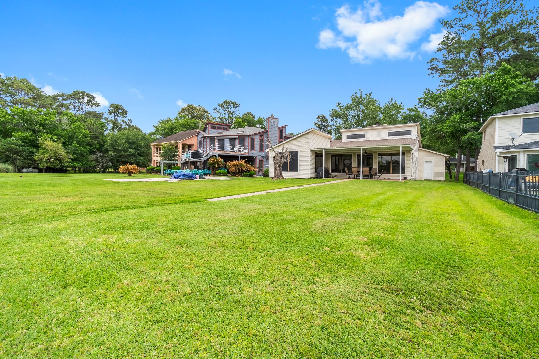 2839 Hemingway Drive Montgomery, TX 77356 - Photo 38 of 49 This photo showcases a spacious backyard with a well-maintained lawn leading up to a contemporary house featuring a large deck and covered patio. The property is surrounded by trees, offering a serene and private setting.