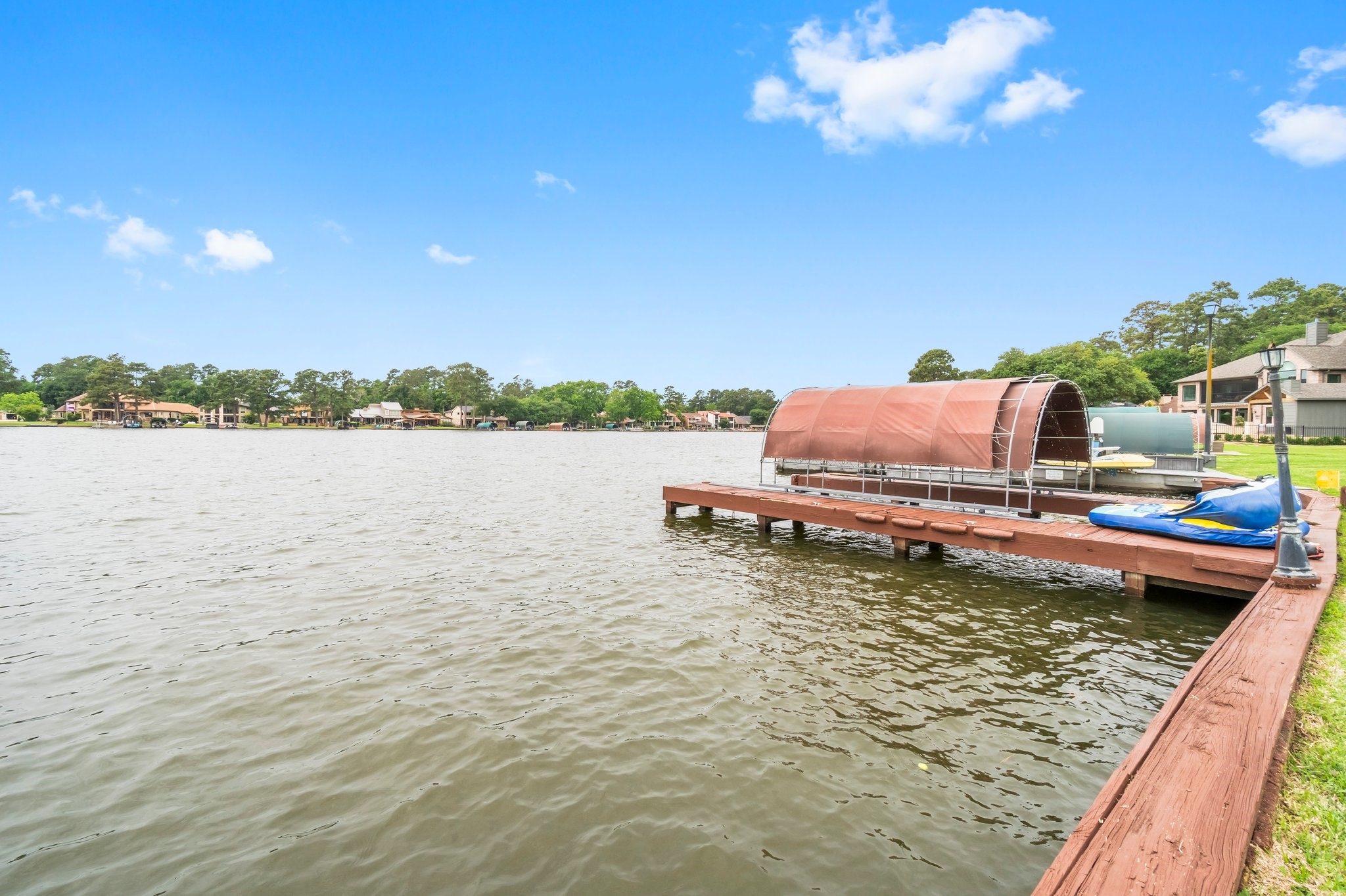 2839 Hemingway Drive Montgomery, TX 77356 - Photo 39 of 49 This photo showcases a lakeside property with a wooden dock and boat cover, offering serene water views and proximity to other waterfront homes. Ideal for boating enthusiasts and those seeking a tranquil lifestyle.