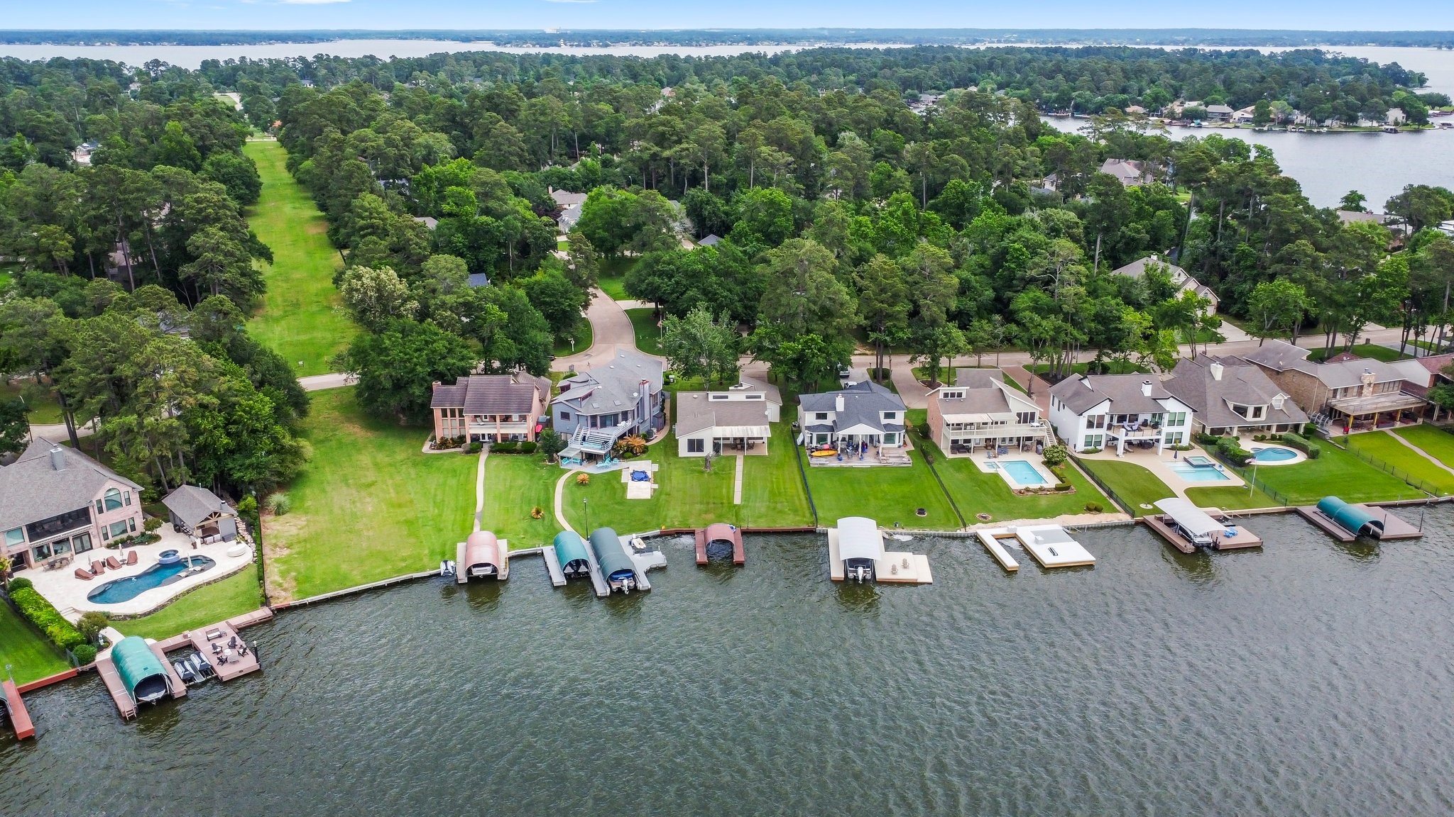 2839 Hemingway Drive Montgomery, TX 77356 - Photo 46 of 49 This photo showcases a beautiful waterfront neighborhood with spacious homes, each featuring private docks on a serene lake. The properties have lush green lawns, some with pools, and are surrounded by a wooded area, offering privacy and scenic views. Perfect for buyers seeking a tranquil, luxurious lifestyle by the water.