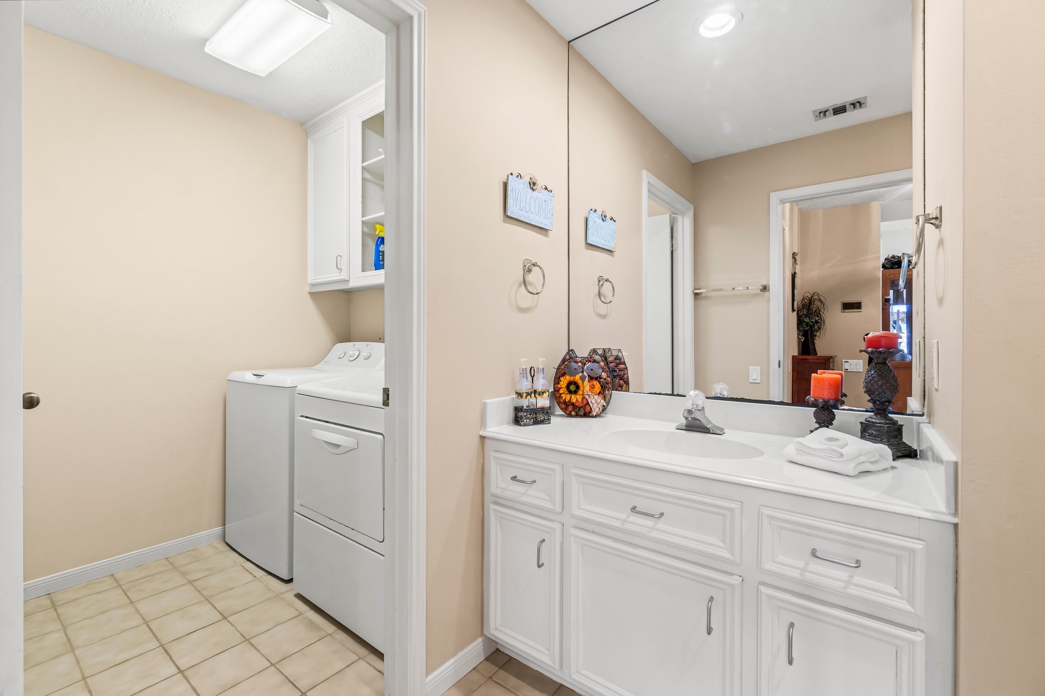 2839 Hemingway Drive Montgomery, TX 77356 - Photo 7 of 49 This photo shows a well-lit bathroom with a large vanity mirror and white cabinetry. Adjacent is a compact laundry area with a washer and dryer, offering convenient access and functionality.