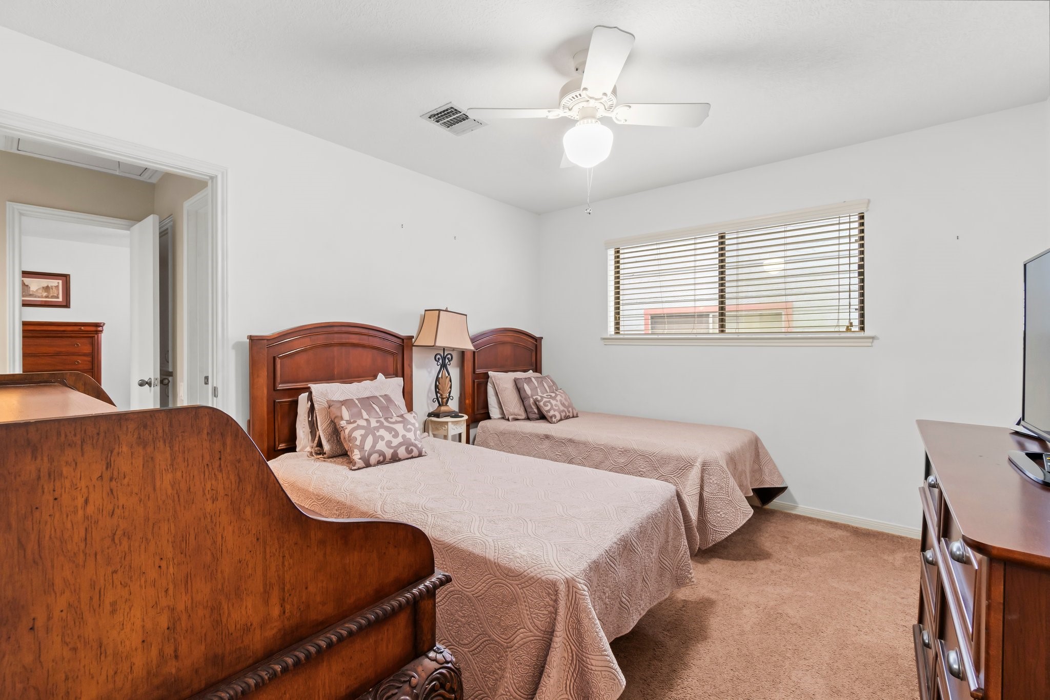2839 Hemingway Drive Montgomery, TX 77356 - Photo 8 of 49 This cozy bedroom features two twin beds with elegant wooden headboards, a ceiling fan, and a window with blinds for natural light. The room has carpeted floors and neutral walls, offering a warm and inviting atmosphere.