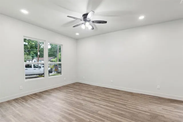 an empty room with wooden floor fan and windows