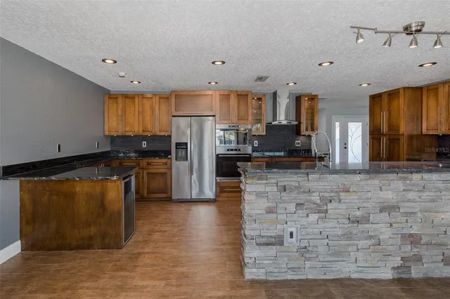 a kitchen with stainless steel appliances granite countertop a refrigerator a stove and a sink with wooden floors