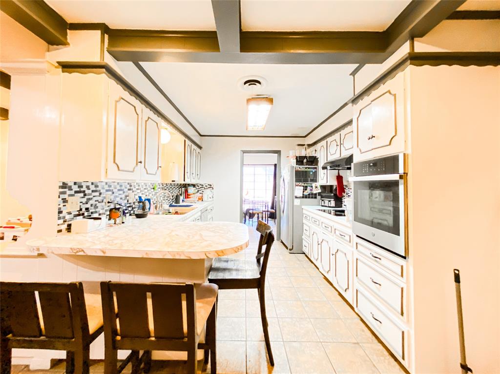 4301 Caprock Road Abilene, TX 79606 - Photo 8 of 29 Galley kitchen featuring white cabinetry with gold trim, a built-in oven, tile flooring, a multi-tone tile backsplash, and a breakfast bar with a stone-finish countertop
