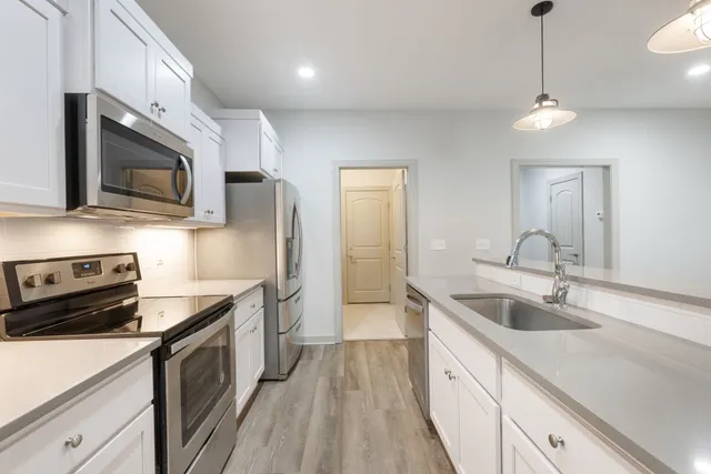 a kitchen with stainless steel appliances a sink a stove oven a refrigerator with white cabinets and wooden floor