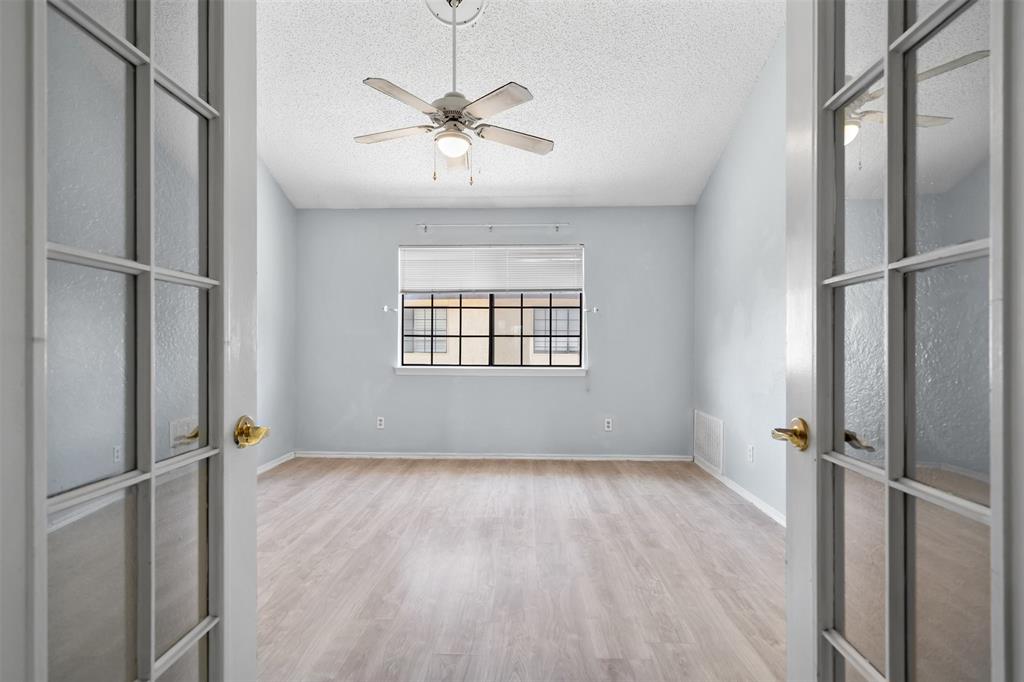 5590 Spring Valley Road, Unit H 203 Dallas, TX 75254 - Photo 18 of 27 French doors open to a room featuring wood-finish flooring, a window with gridded panes, and a ceiling fan with integrated lighting