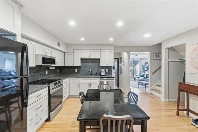 a kitchen with stainless steel appliances granite countertop a stove top oven a sink a refrigerator white cabinets and chairs