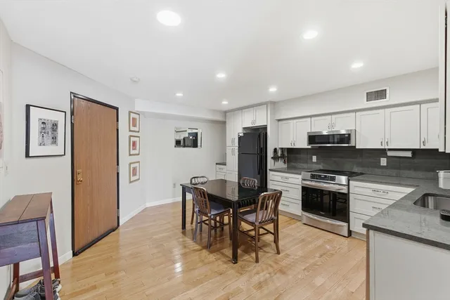 a kitchen with stainless steel appliances granite countertop a stove a refrigerator a kitchen island a dining table and chairs with wooden floor