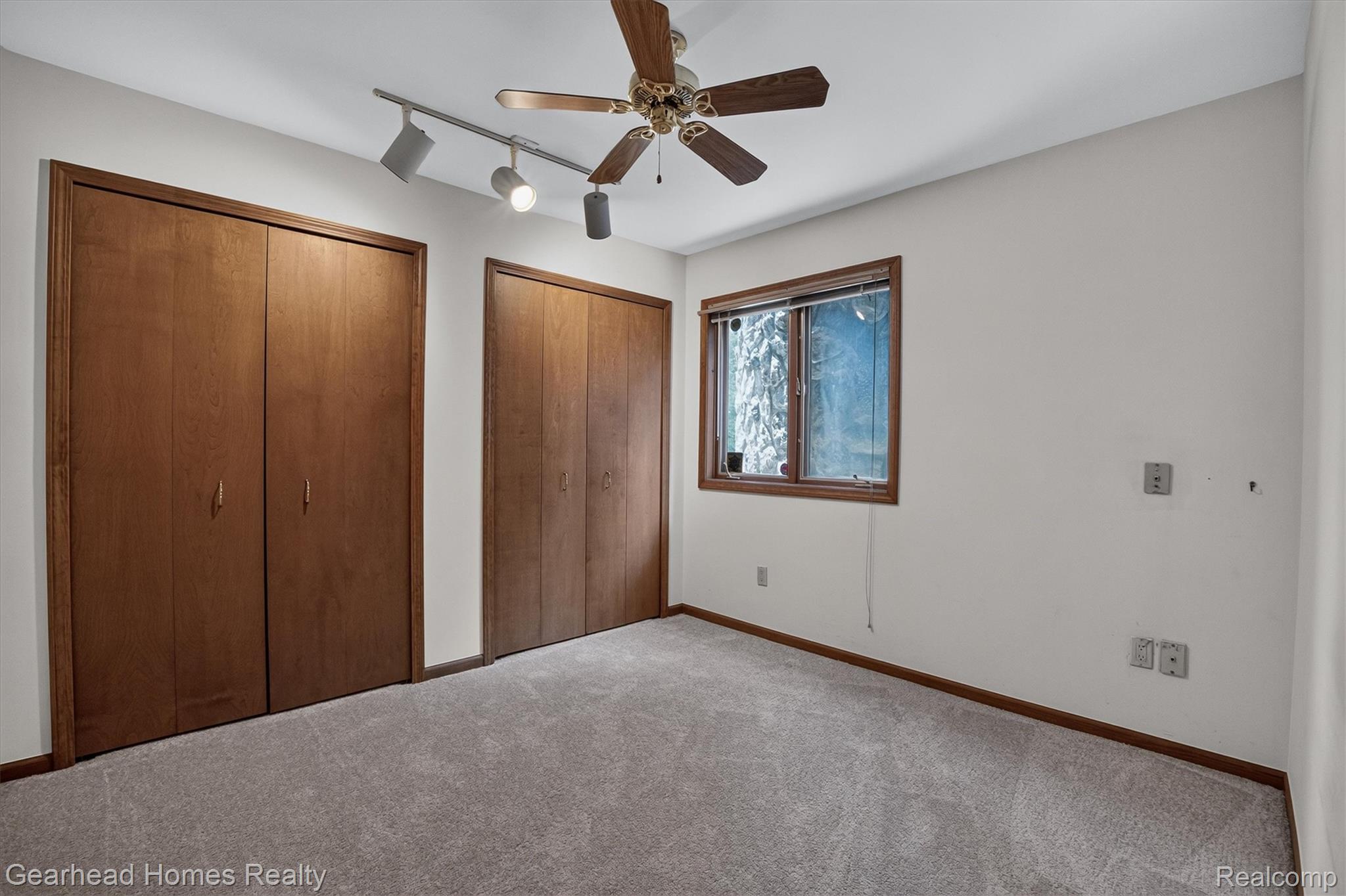 3486 West Drahner Road Oxford, MI 48371 - Photo 14 of 51 Carpeted room featuring two wood-finish bi-fold closets, a window with wood trim, a ceiling fan, and track lighting