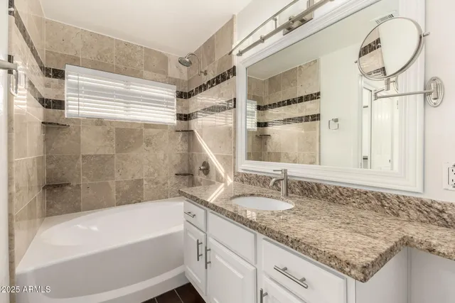 a bathroom with a granite countertop sink and mirror with bathtub