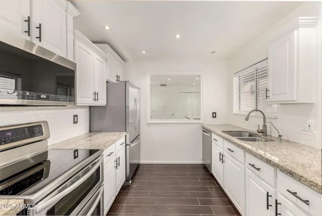 a white kitchen with stainless steel appliances granite countertop a sink and dishwasher a stove top oven with wooden floor