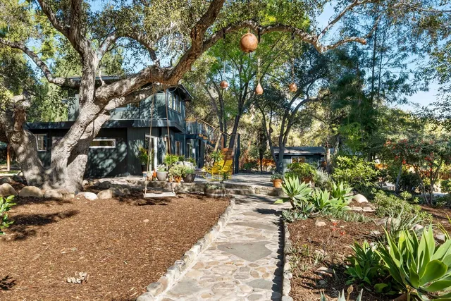 a backyard of a house with table and chairs under a large tree