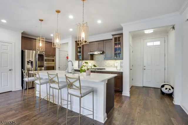 a kitchen with stainless steel appliances kitchen island granite countertop a stove a refrigerator a oven a dining table and chairs with wooden floor