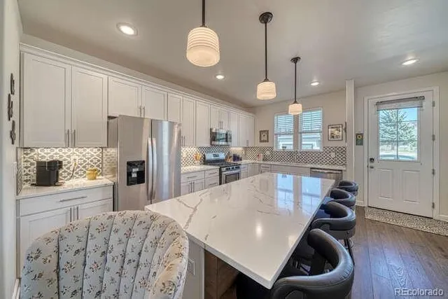 a kitchen with stainless steel appliances granite countertop a sink a stove a refrigerator cabinets and chairs