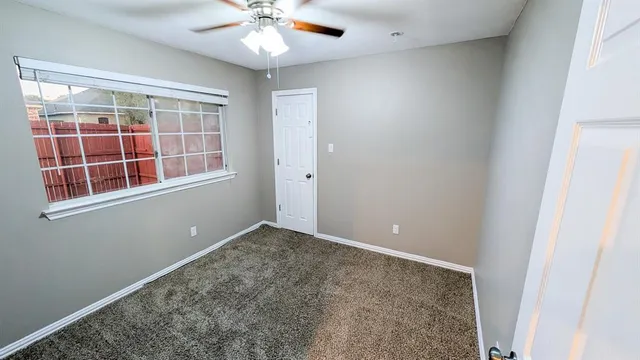 an empty room with a chandelier fan and windows