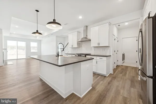 a kitchen with stainless steel appliances granite countertop a sink a stove a refrigerator and white cabinets with wooden floor