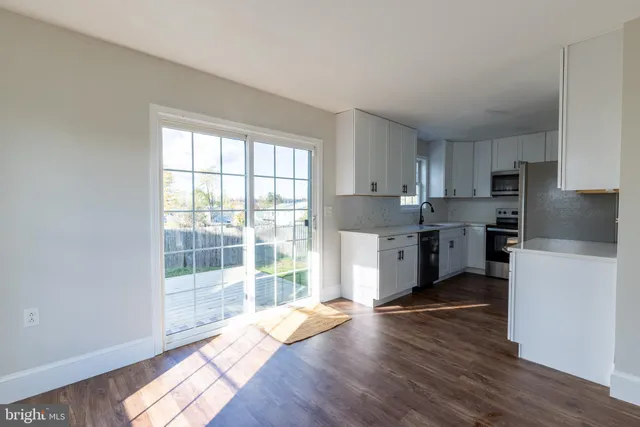 a kitchen with granite countertop a refrigerator a sink a stove and white cabinets with wooden floor