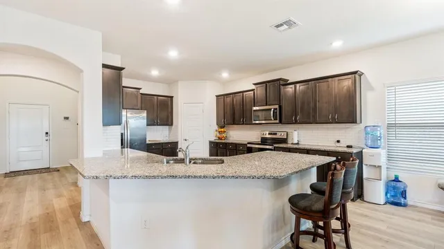 a kitchen with stainless steel appliances granite countertop a sink a stove a refrigerator cabinets and chairs